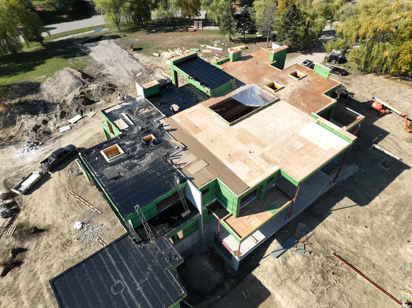 Aerial view of a Brampton building under construction with plywood roof decking, black membrane sections, green wall sheathing and ladders