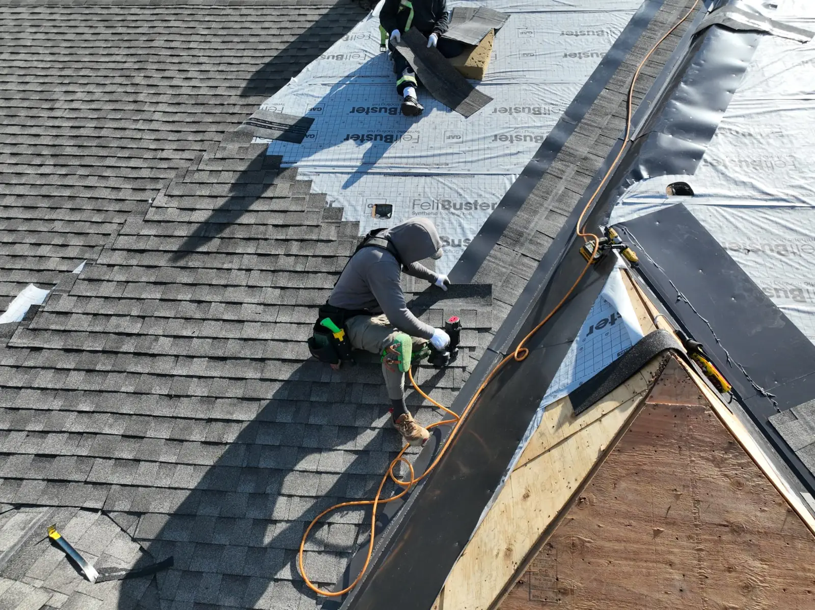 Overhead view of roofers installing grey shingles beside silver underlayment on an Oakville home