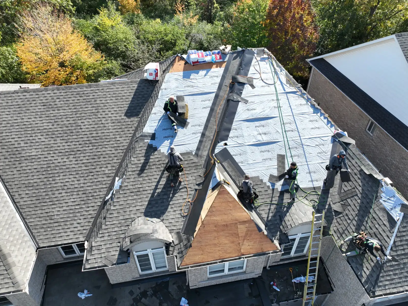 Wide drone view of an Oakville roof installation with workers, underlayment and autumn trees