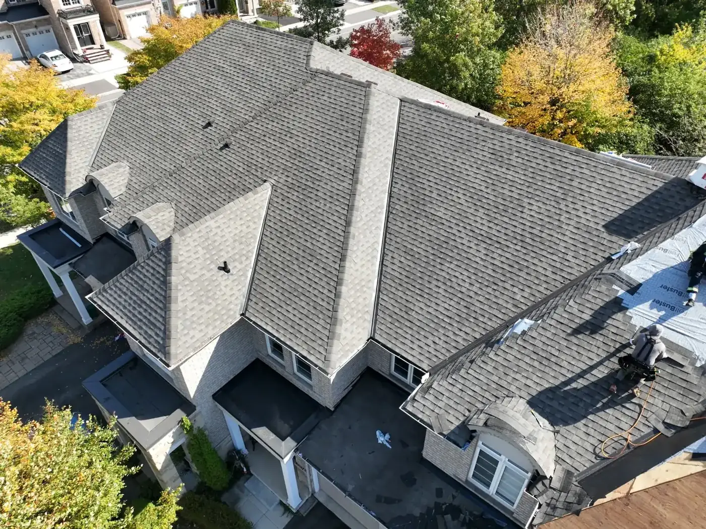 Aerial drone view of a nearly completed Oakville roof with fresh grey shingles and autumn trees behind the property