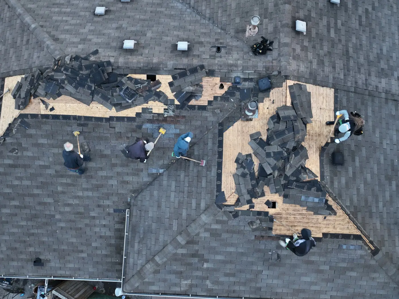 Top-down drone view of the Ontario Tech Roofing crew tearing off old shingles on a Mississauga roof, with piles of removed shingles and exposed plywood decking across the slopes