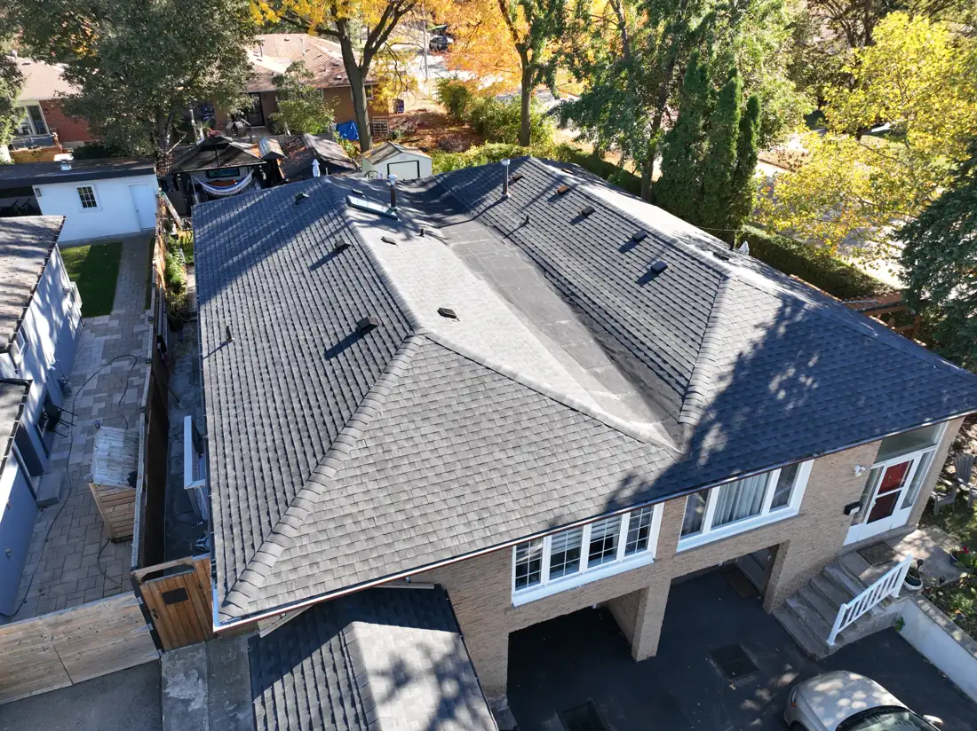 Drone view of the completed charcoal shingle roof on a Mississauga detached house on Bonnymede Drive, seen from the front with autumn trees behind