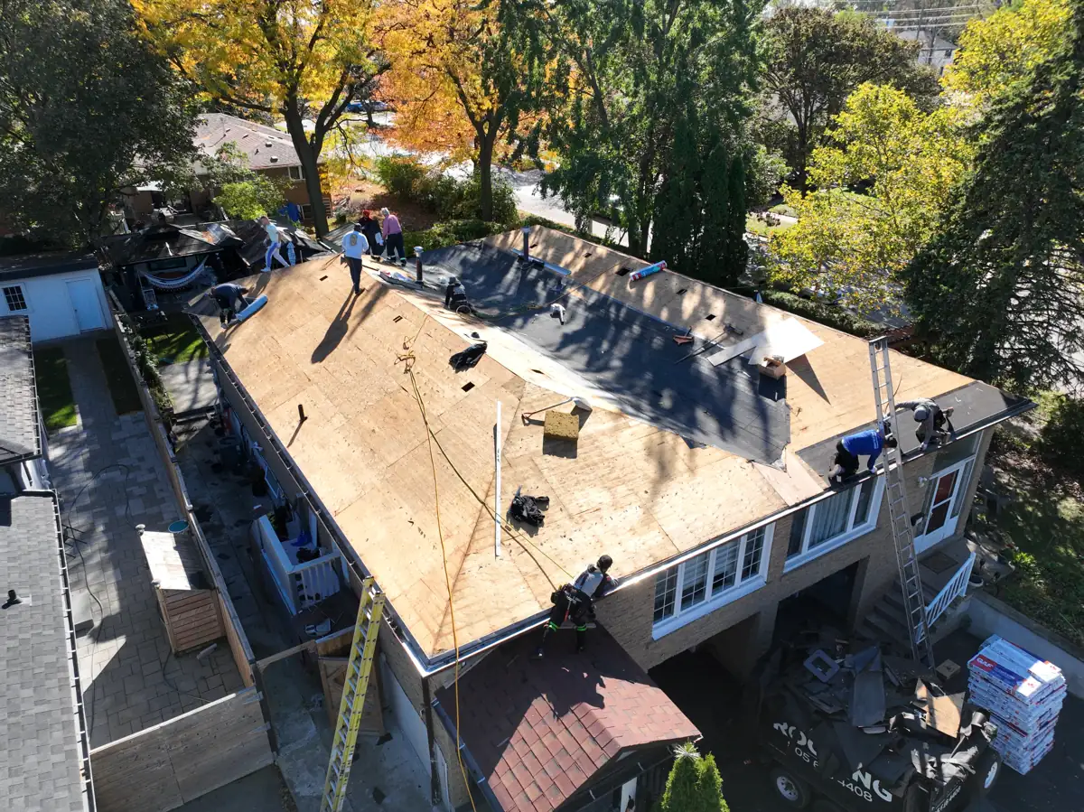 Aerial view of a Mississauga roof replacement with the old shingles removed, exposed decking, ice and water shield on the lower roof and GAF shingle bundles staged on the driveway