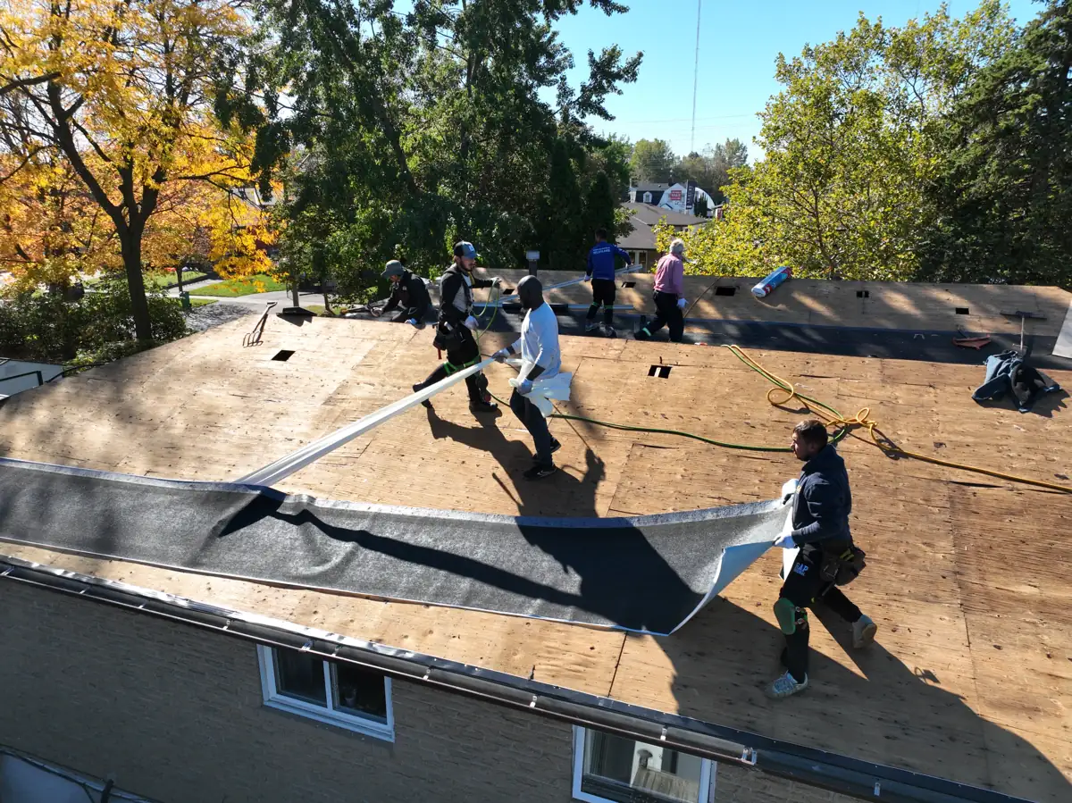 Roofers rolling out ice and water shield along the eaves of a Mississauga home over new plywood decking
