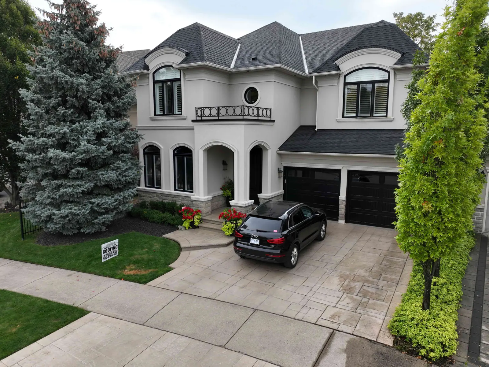 Drone view of a completed two-storey Oakville home with a dark charcoal shingle roof, light stucco walls and an Ontario Tech Roofing lawn sign in the front yard